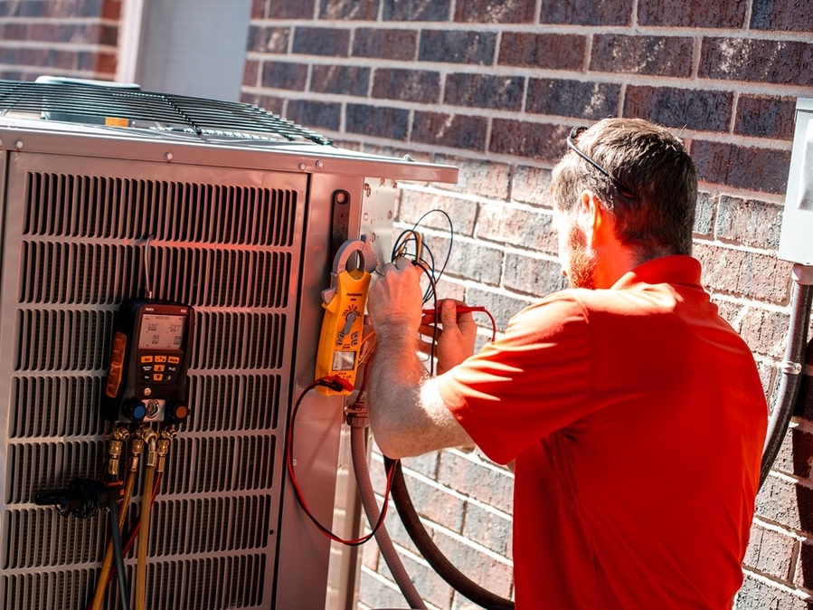 HVAC technician performing maintenance on air conditioning unit, checking gauges and connections in preparation for Texas summer heat.
