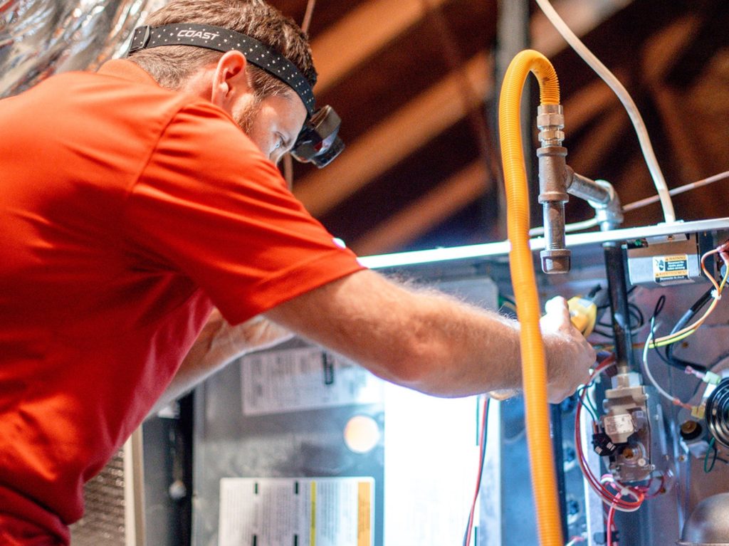HVAC technician in red shirt repairing heating system components, focusing on efficiency and maintenance for Austin homes.