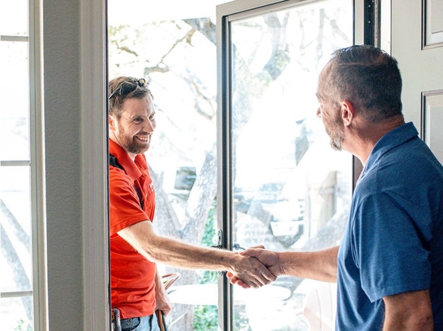 Technician in red shirt greeting homeowner at the door, emphasizing AC repair services in Austin.