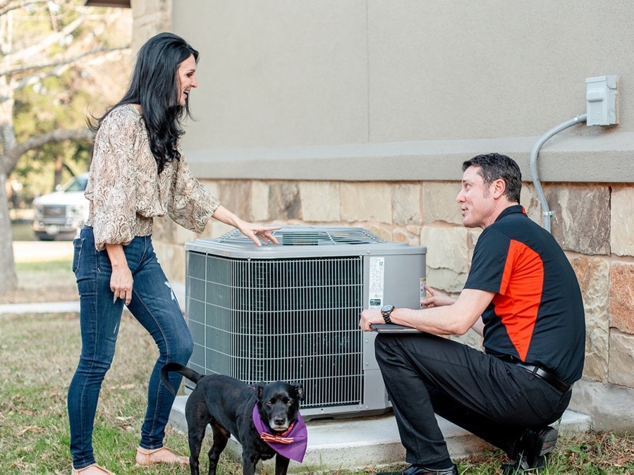 Woman consulting with HVAC technician beside air conditioning unit, dog nearby, highlighting AC maintenance and repair discussion.